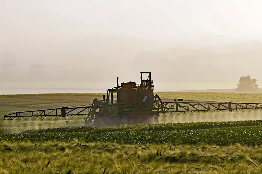 Foliar fertilizer application, tractor boom sprayer applying liquid nutrients over a crop